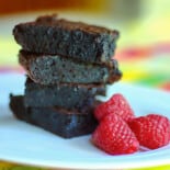 side view of stacked fudge brownies on white dish with raspberries
