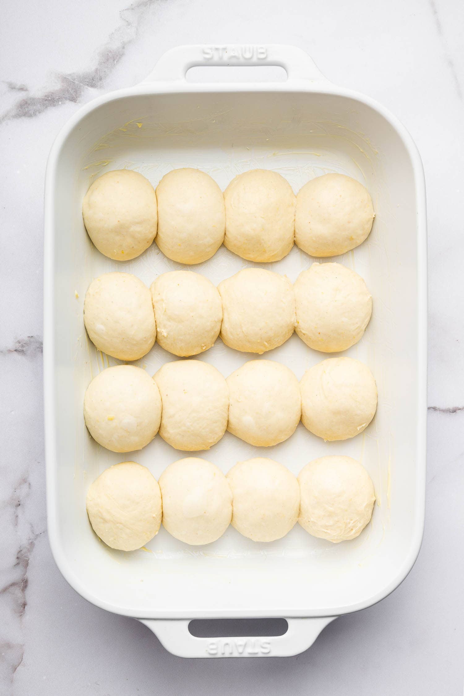 Fluffy raw dough balls in a white baking dish for baking bread or rolls.