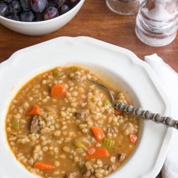 beef barley soup in white bowl with spoon on wooden background