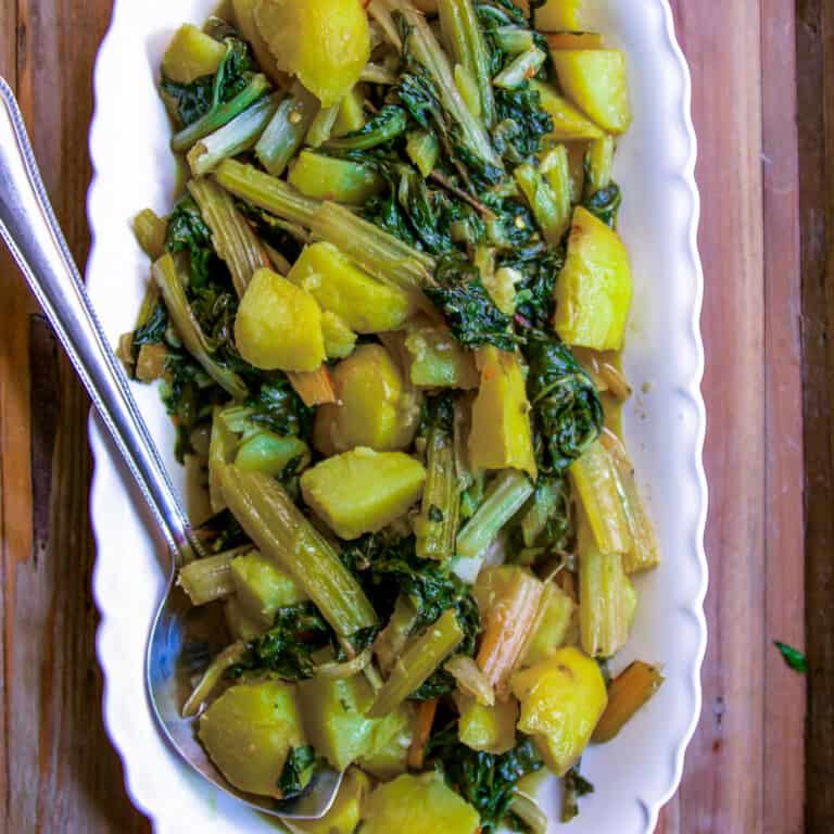 top view of swiss chard with potatoes on white dish with spoon