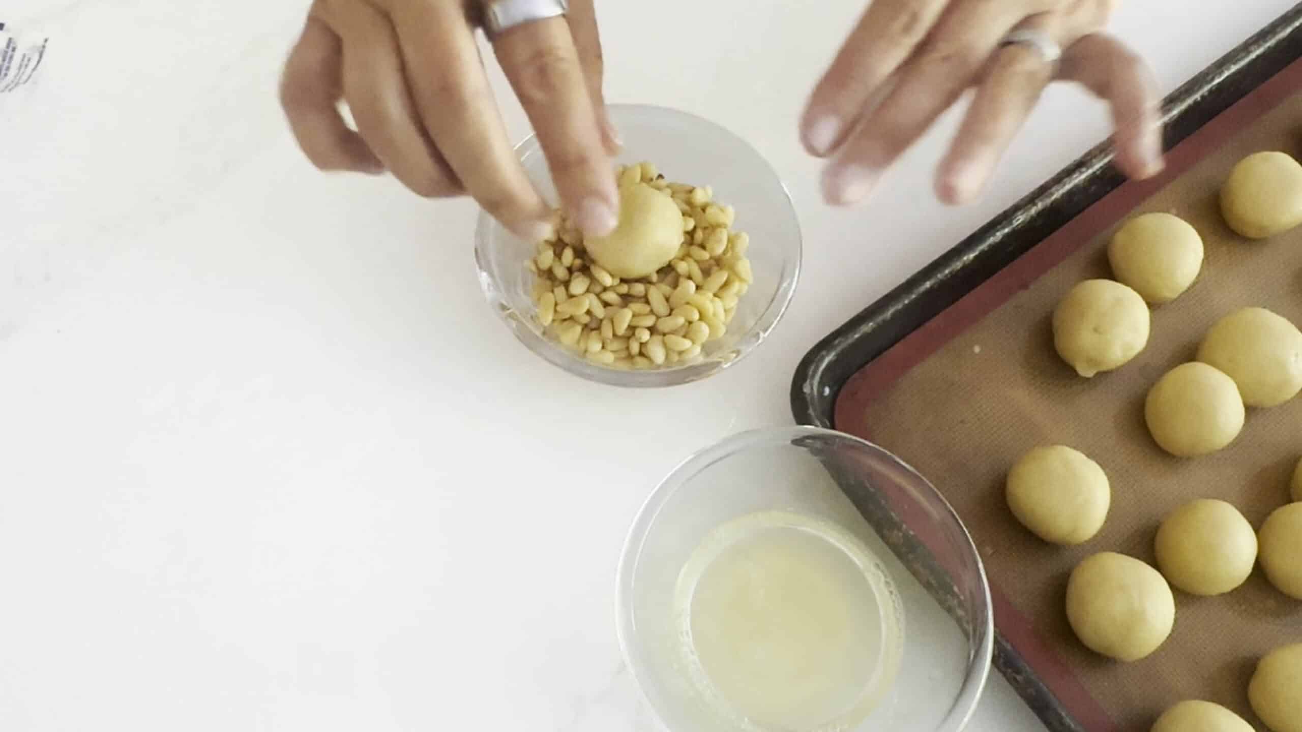 Dipping cookie balls into pine nuts. 