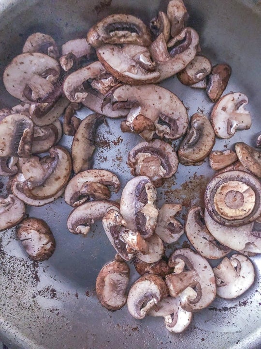 pan of raw sliced mushrooms cooking on stovetop