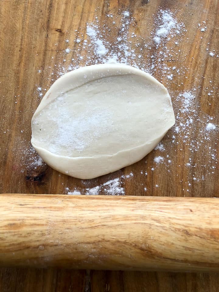 Flattened piece of dough on floured wooden board. 