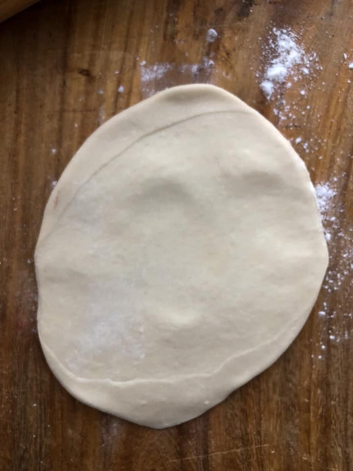 Dough flattened further on wooden board. 
