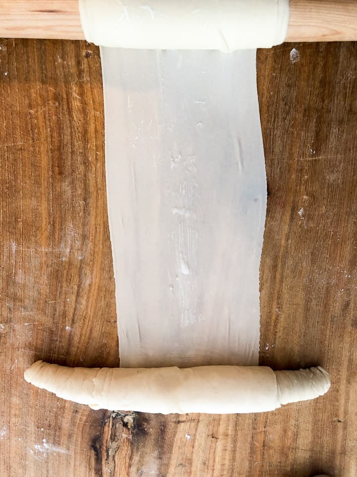 Rolling thin dough into a cylinder shape from the rolling pin, which staged the dough. 