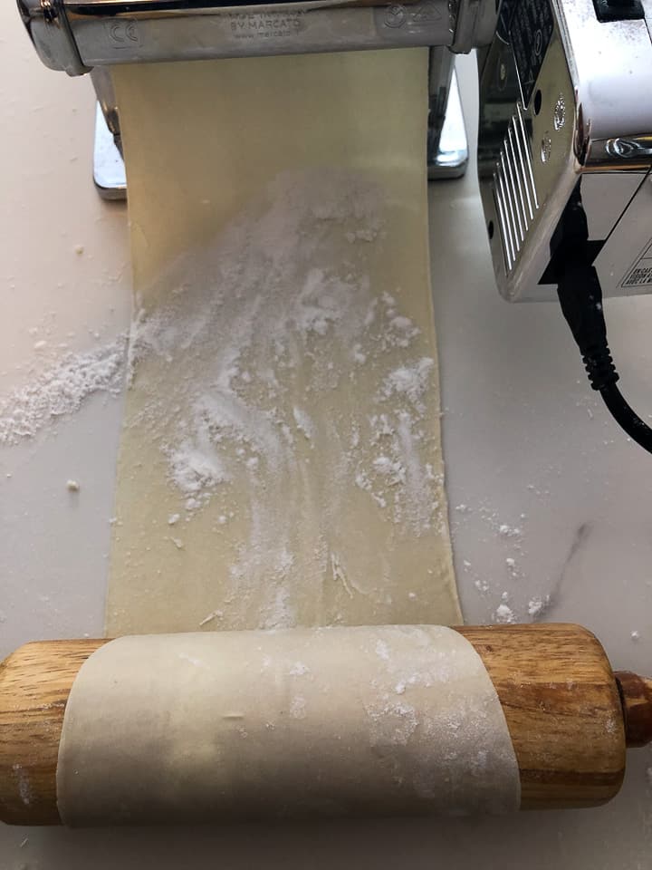 Dough passing through pasta machine and being rolled up on rolling pin. 