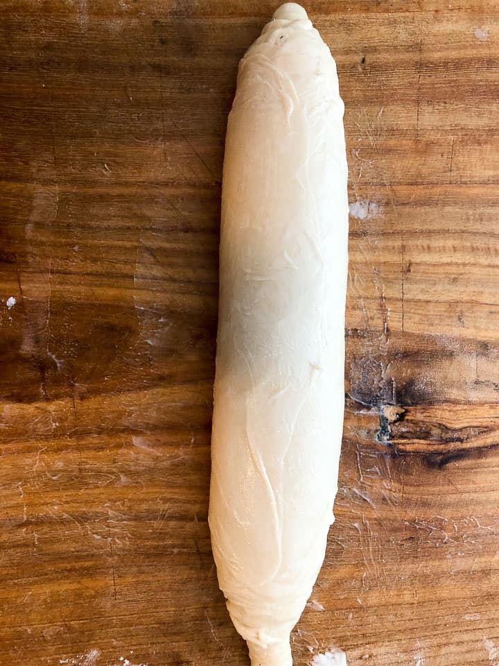 The roll of dough all finished on the wooden board. 