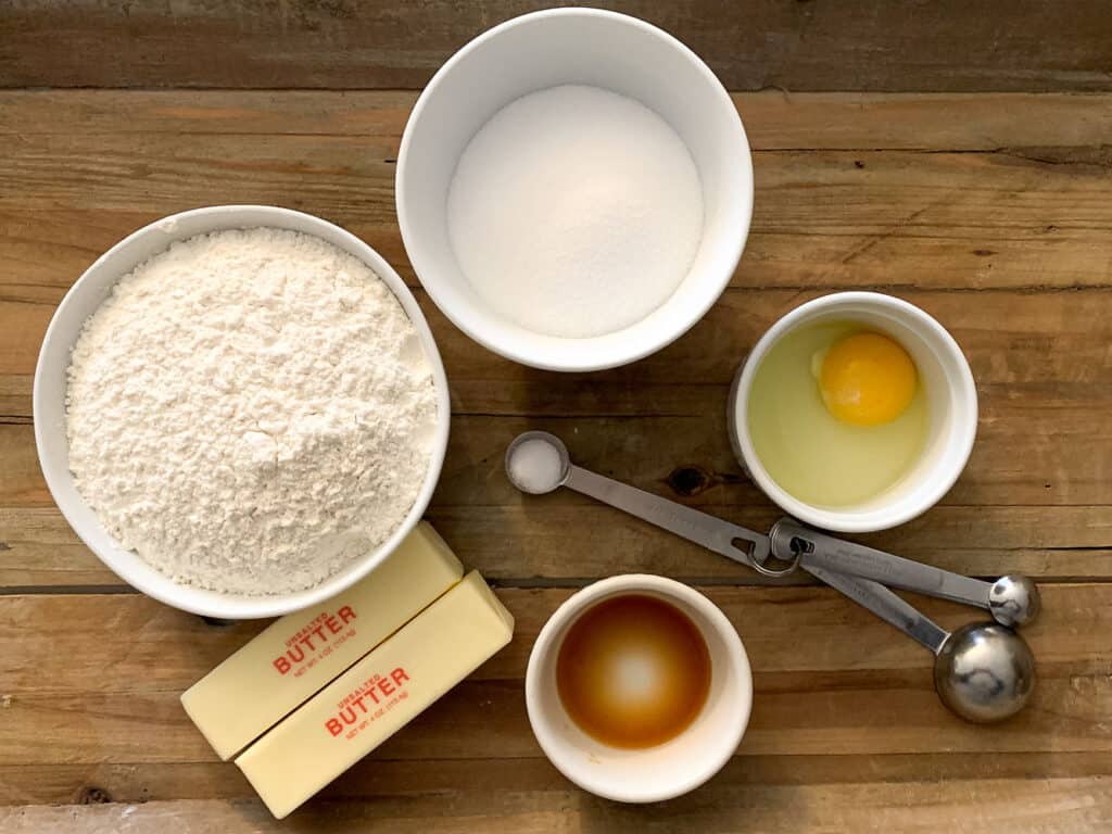 overhead view of sugar cookie dough ingredients including flour, butter, sugar, egg, salt, and vanilla extract