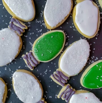 overhead view of sugar cookies shaped like Christmas tree lights on black tray