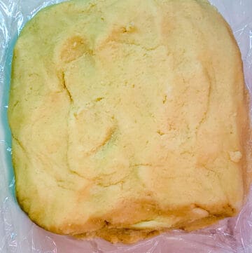 Raw sugar cookie dough shaped into a flattened block on top of plastic wrap