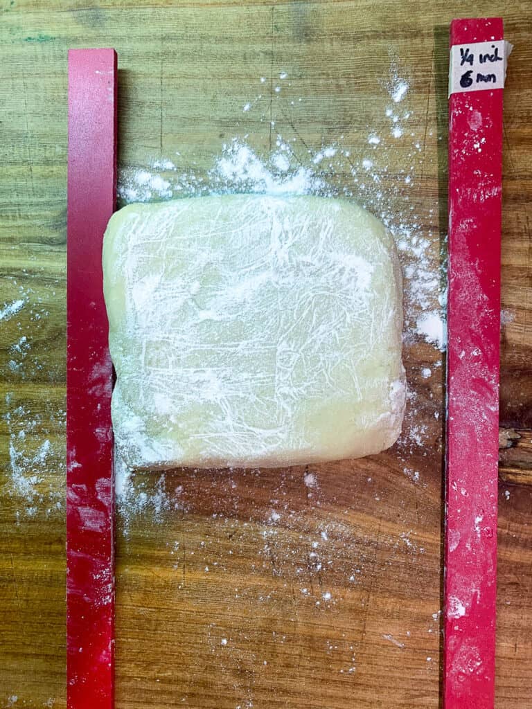 block of sugar cookie dough on wooden surface with red ¼ guide rales on either side