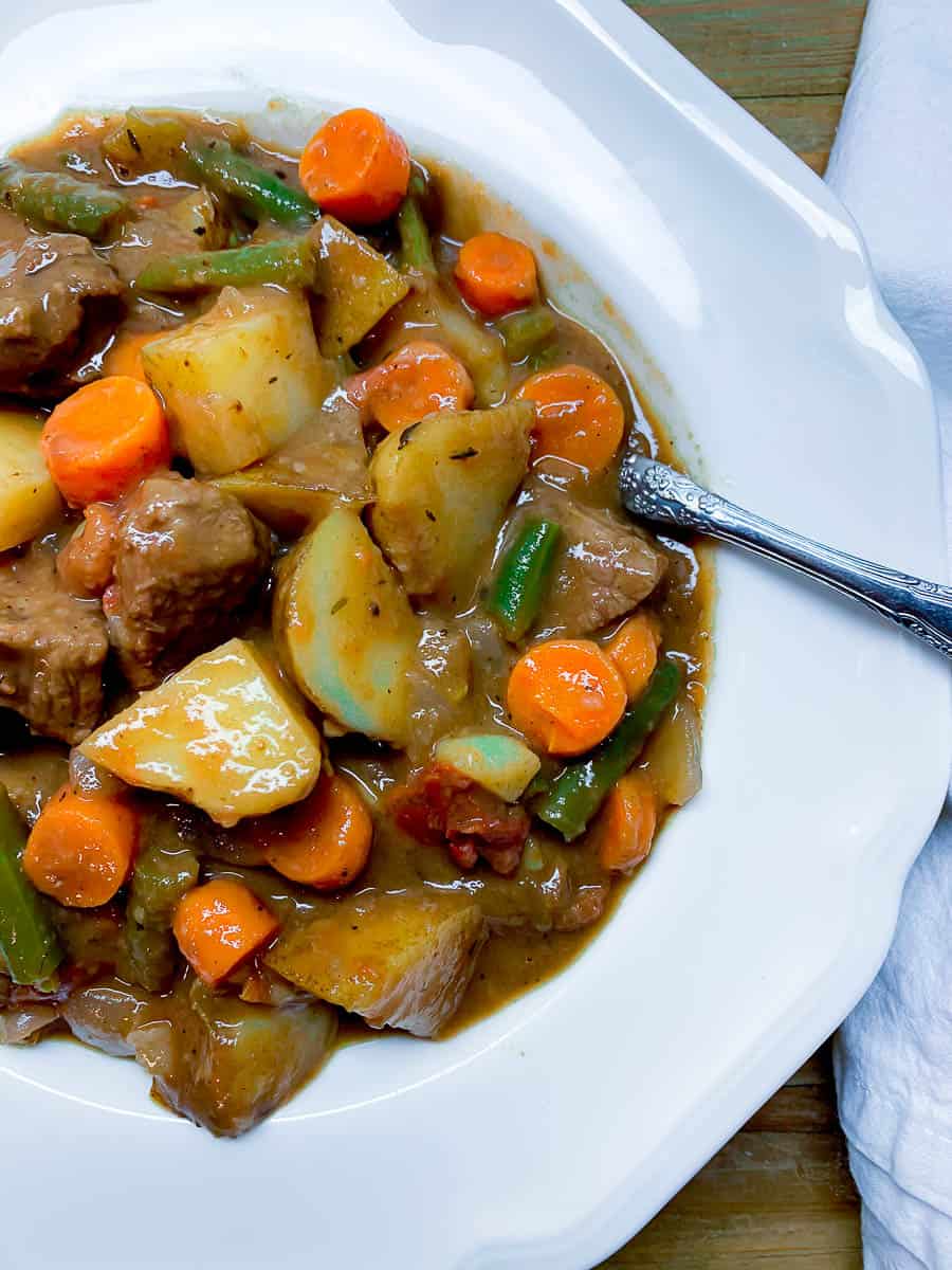 overhead close up view of red wine beef stew in white bowl with spoon