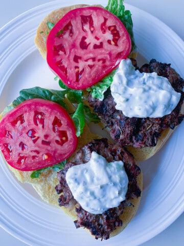 two open faced gyro burgers with tomato and lettuce on white place