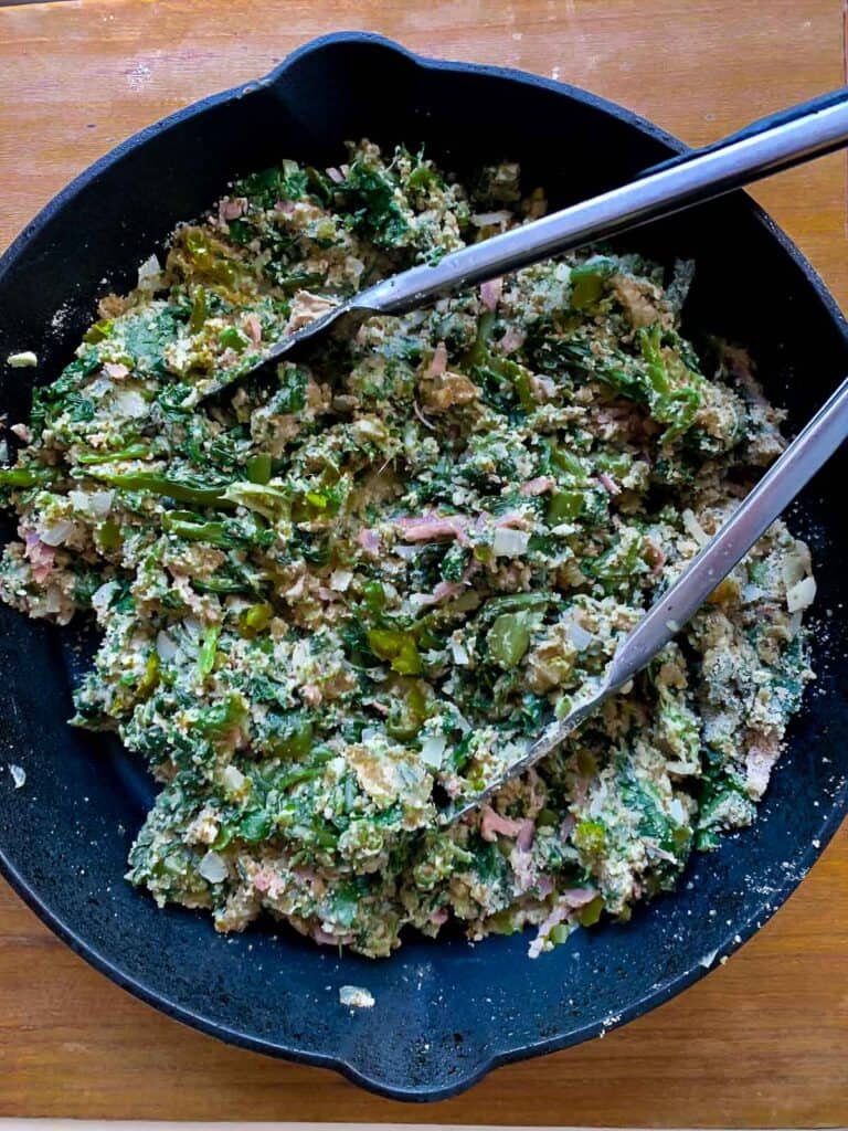 top view of utica greens with tongs in black pan on wooden tabletop