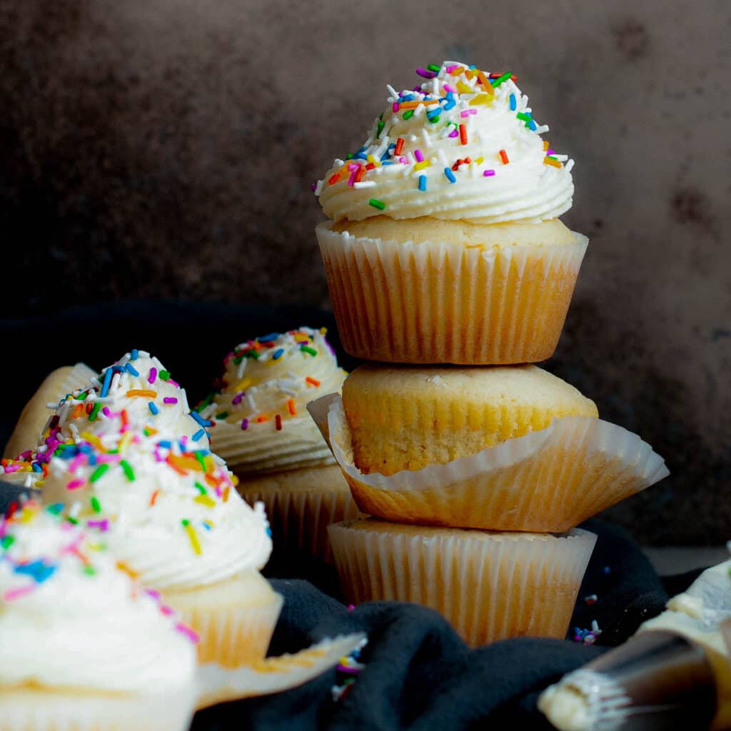 side view of stacked vanilla frosted cupcakes with black background
