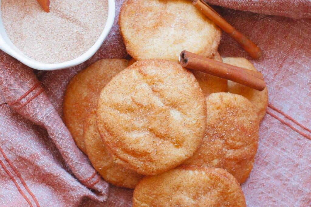 handful of snickerdoodles on purple cloth with cinnamon sticks