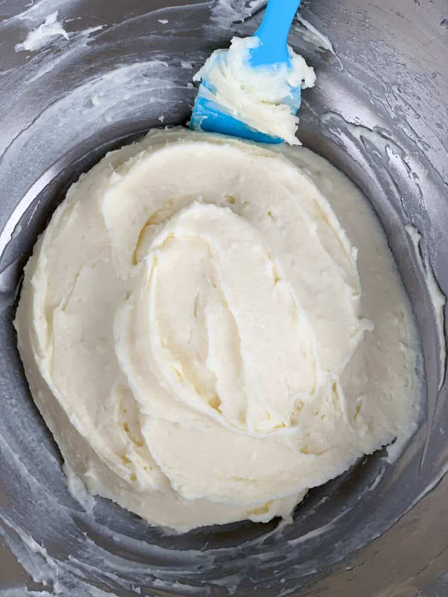 cream cheese frosting in metal bowl with blue spatula