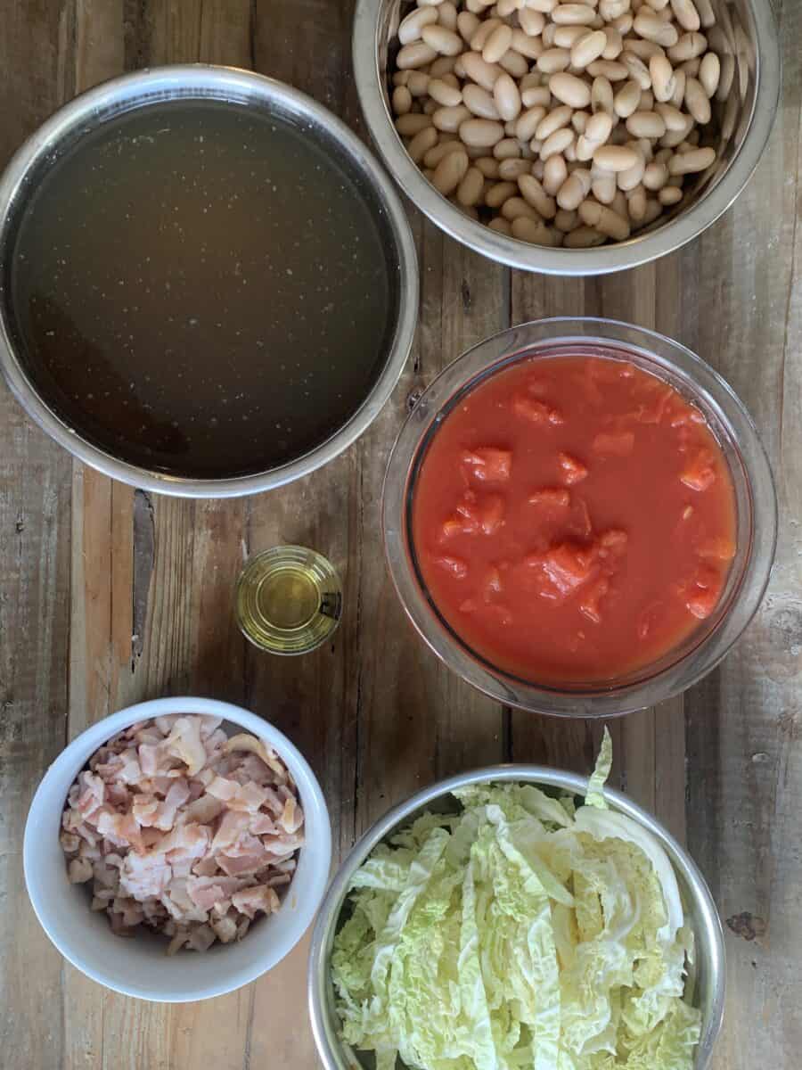 minestrone ingredients, measured out in bowls: cannelloni beans, chicken broth, tomatoes and sauce, olive oil, bacon, sliced cabbage
