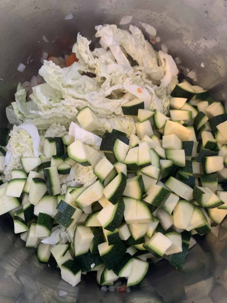 chopped cabbage, zucchini, being added to pot for minestrone