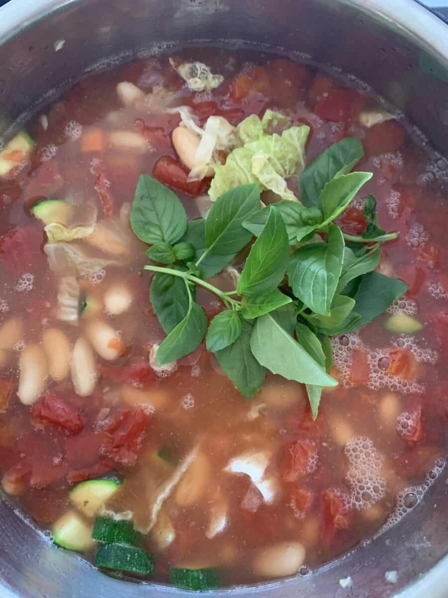 Overhead view of minestrone cooking in pot, topped with fresh basil