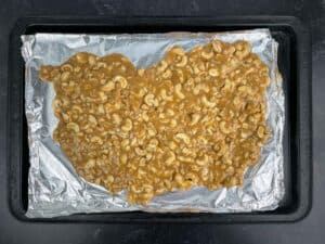 homemade cashew brittle cooling on aluminum foiled lined baking sheet