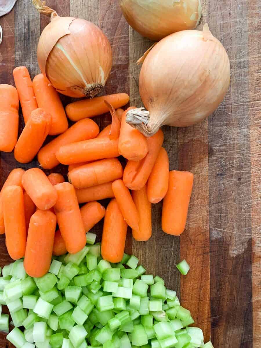 carrots, onion, and celery on wooden cutting board