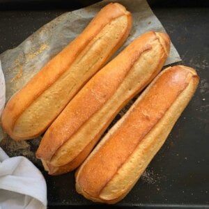 three hoagie rolls on black baking sheet