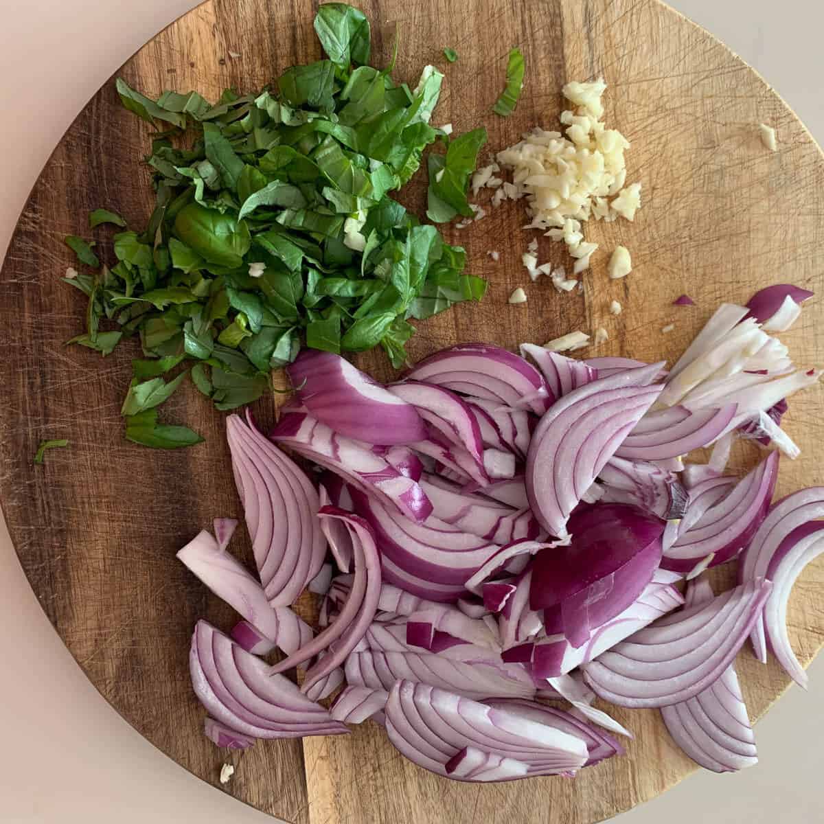 wooden cutting board with basil, red onion and garlic