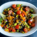black bean and corn salad in white serving bowl with wooden spoons