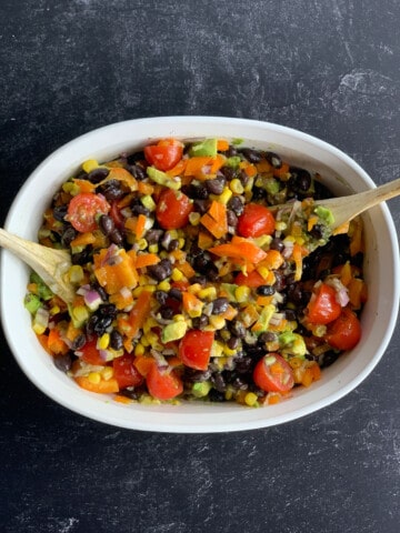 top view of white dish with black bean corn salsa with wooden spoons