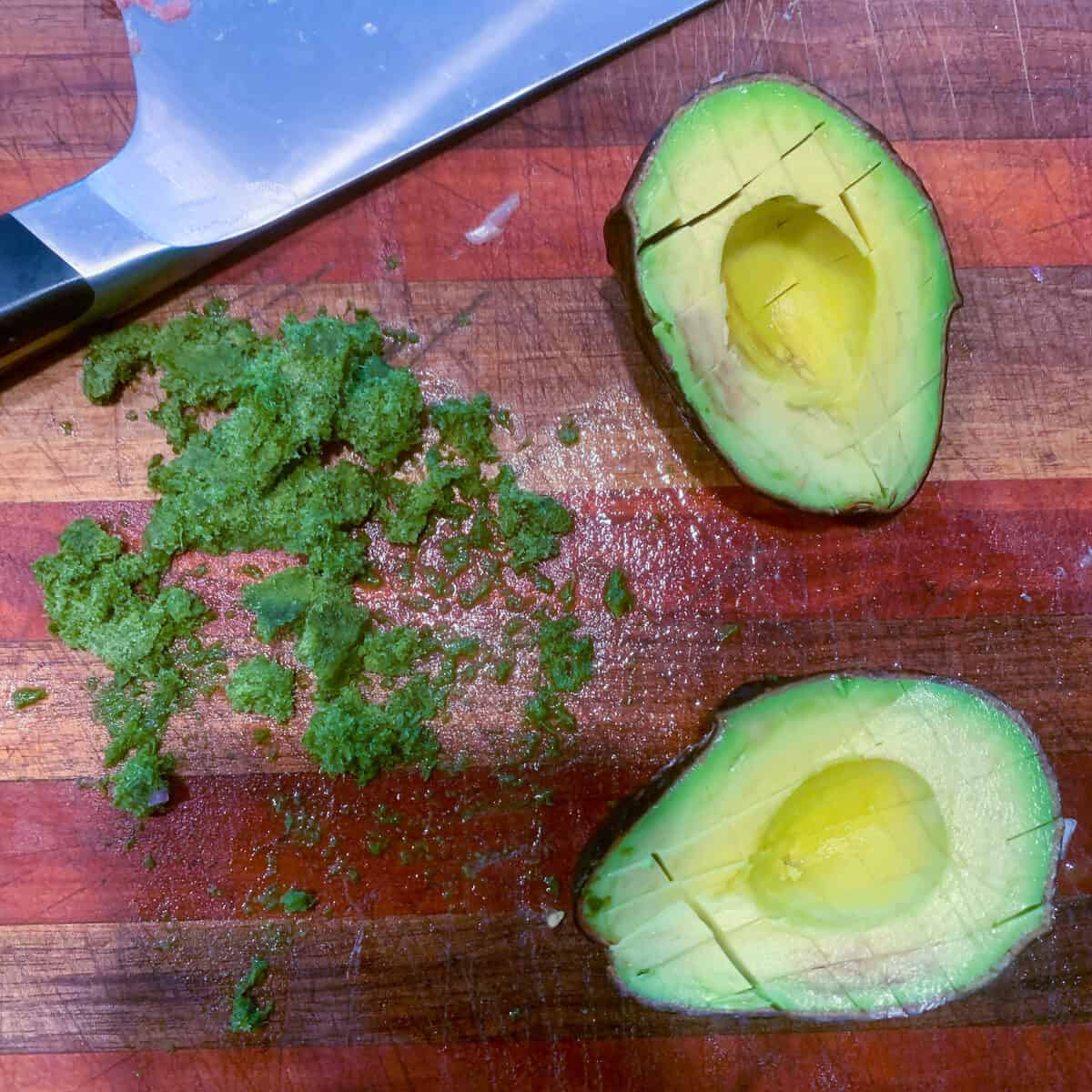 sliced avocado and frozen cilantro on wooden board with knife