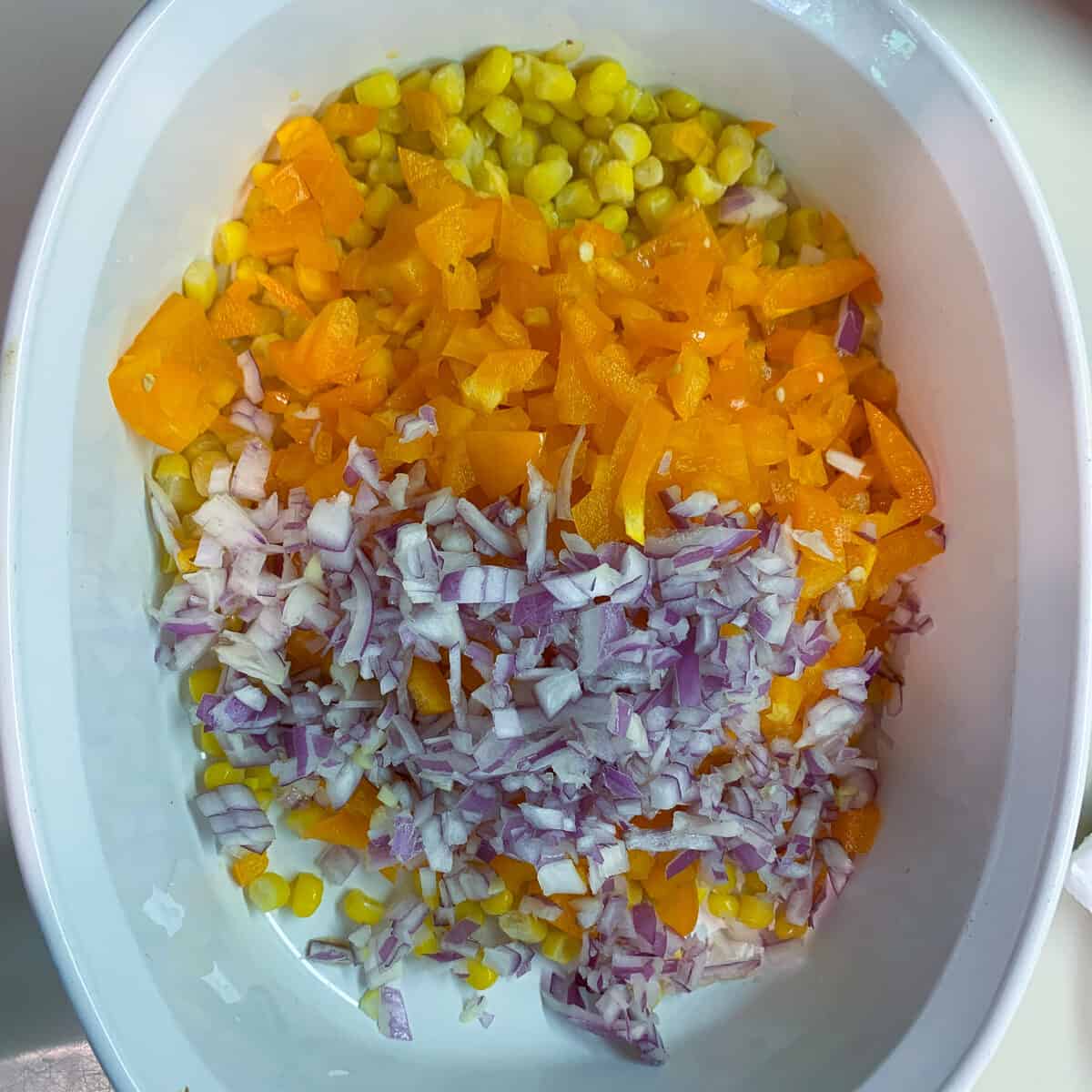 white serving bowl with corn, orange pepper, red onion