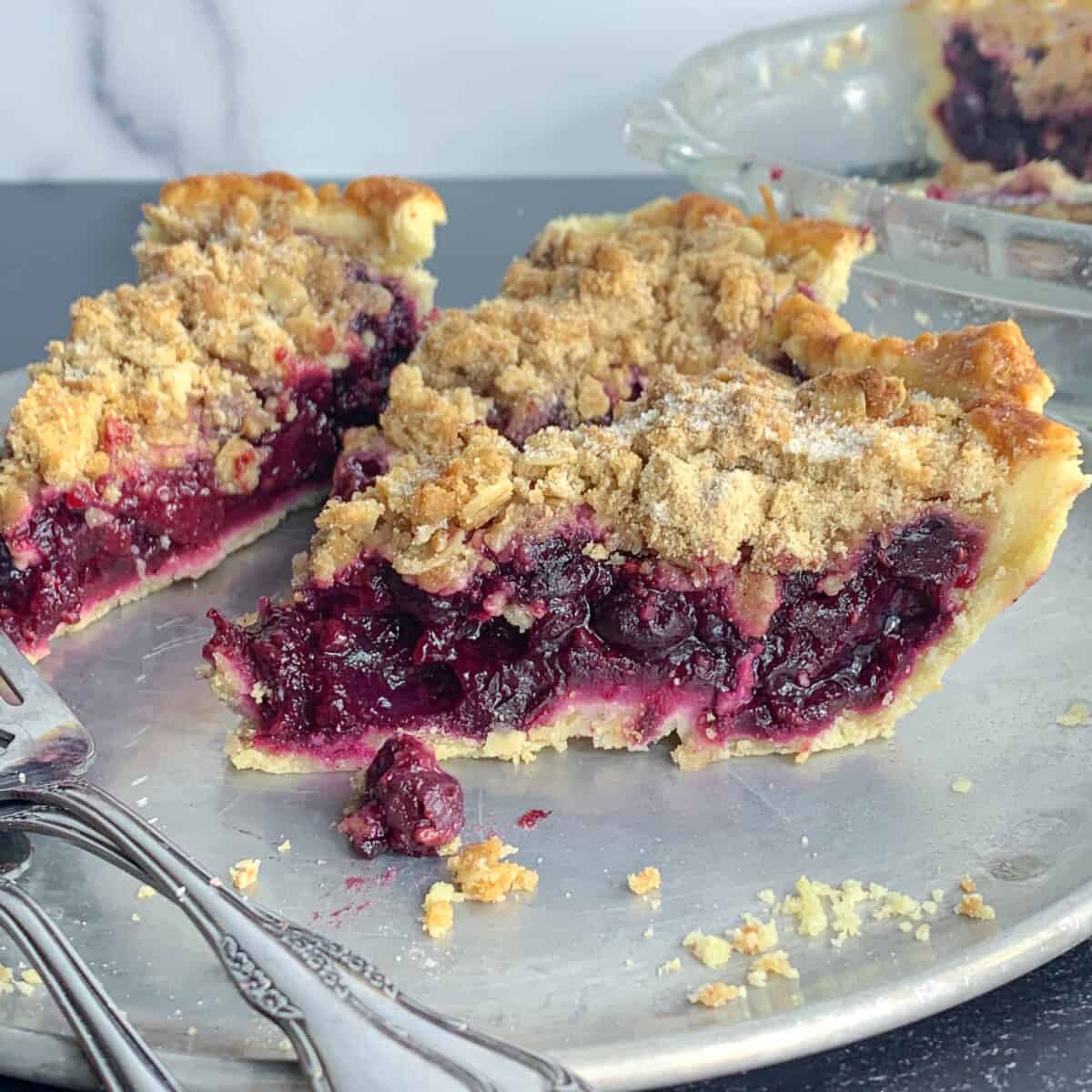 side view of 3 slices of mixed berry pie on silver dish with forks