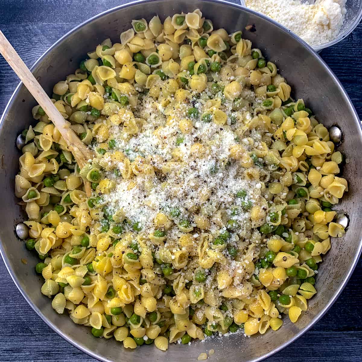 large pan of pasta with peas with wooden on grey table