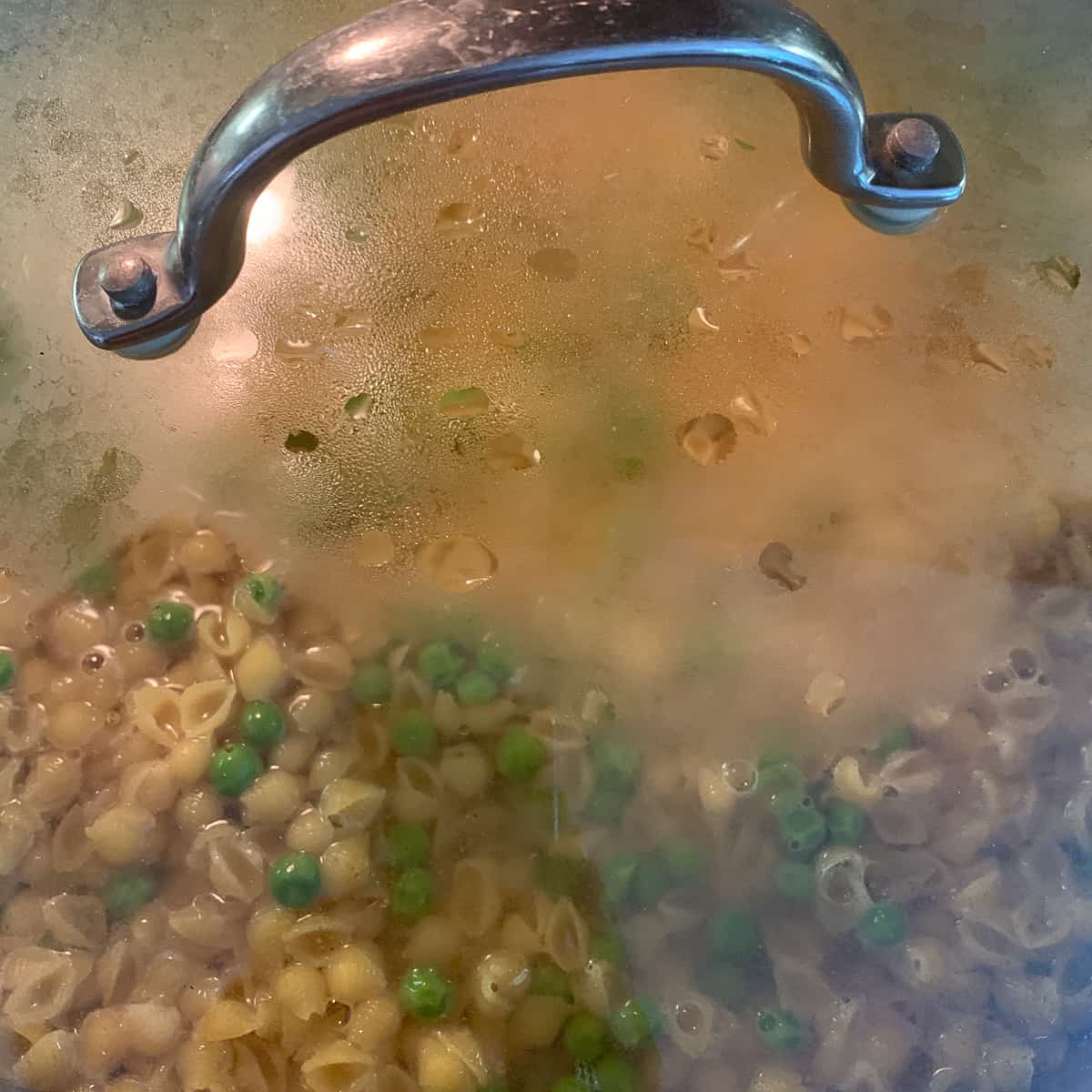 pasta with peas in covered pan cooking on stove