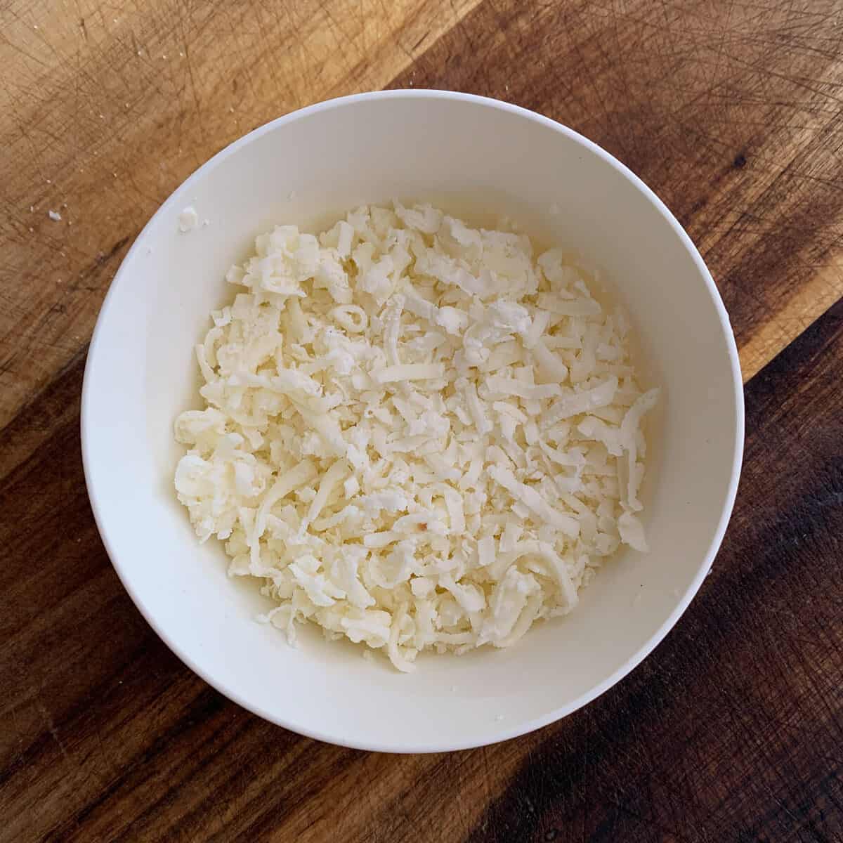 White bowl with shredded cheese on wooden background