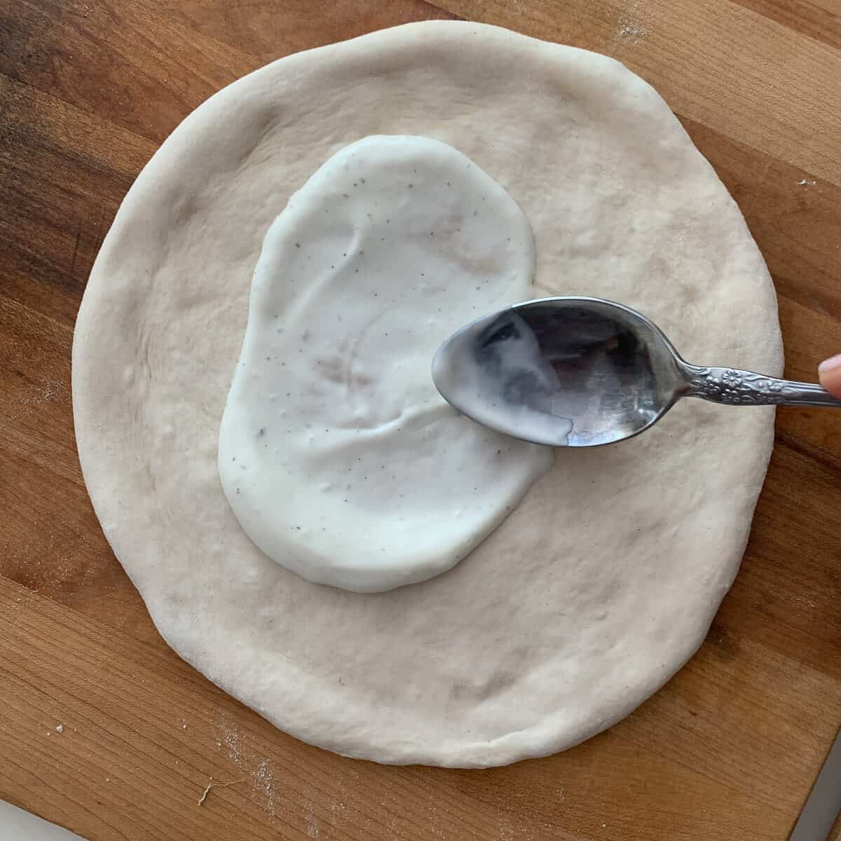 Spreading ranch dressing on pizza dough with spoon