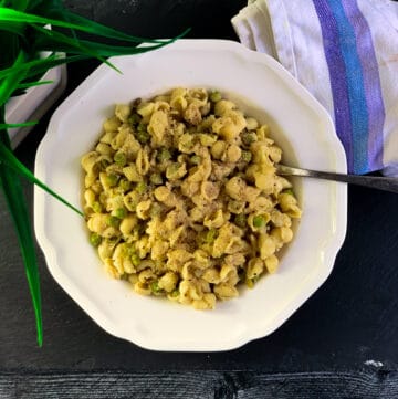 top view of pasta with peas in white bowl with spoon and white purple napkin