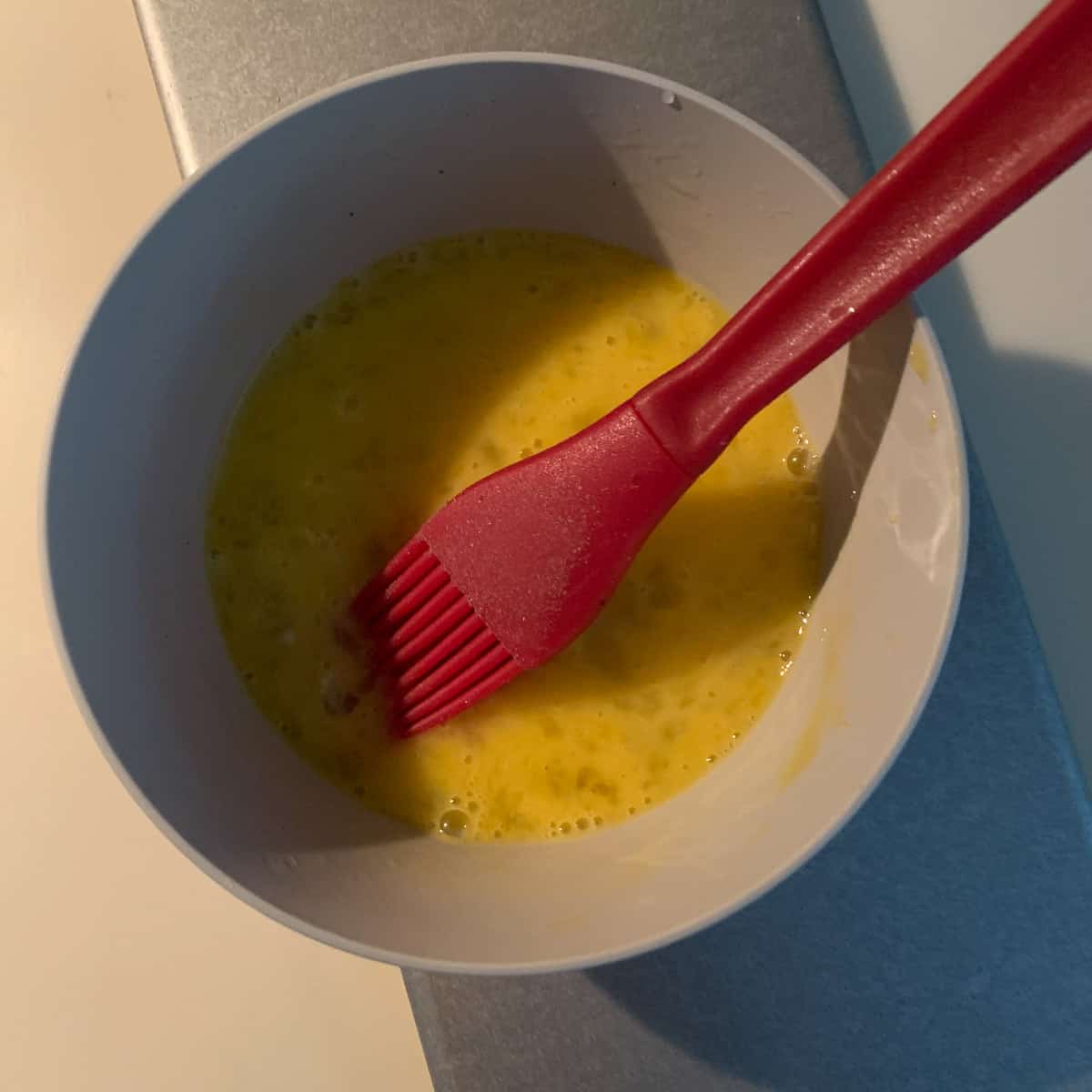 top view of egg wash in small bowl with red brush