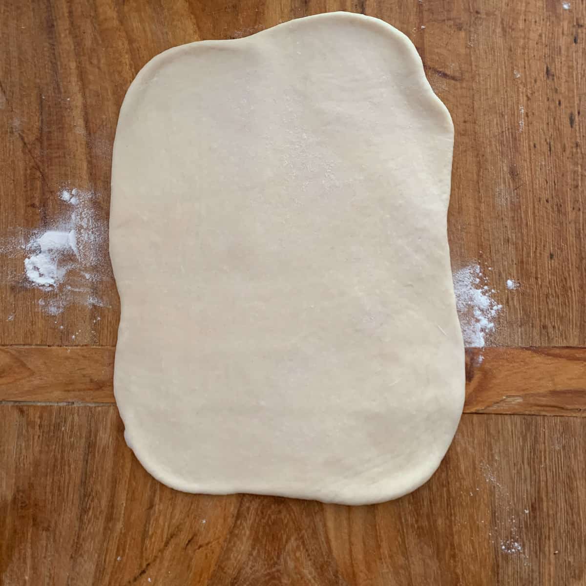 a portion of bread dough rolled out on wooden board