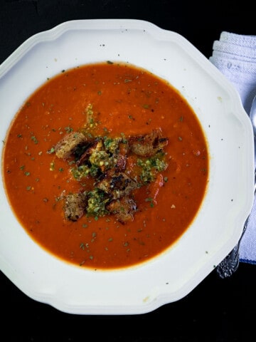 top view of tomato soup with pesto in white bowl with spoon