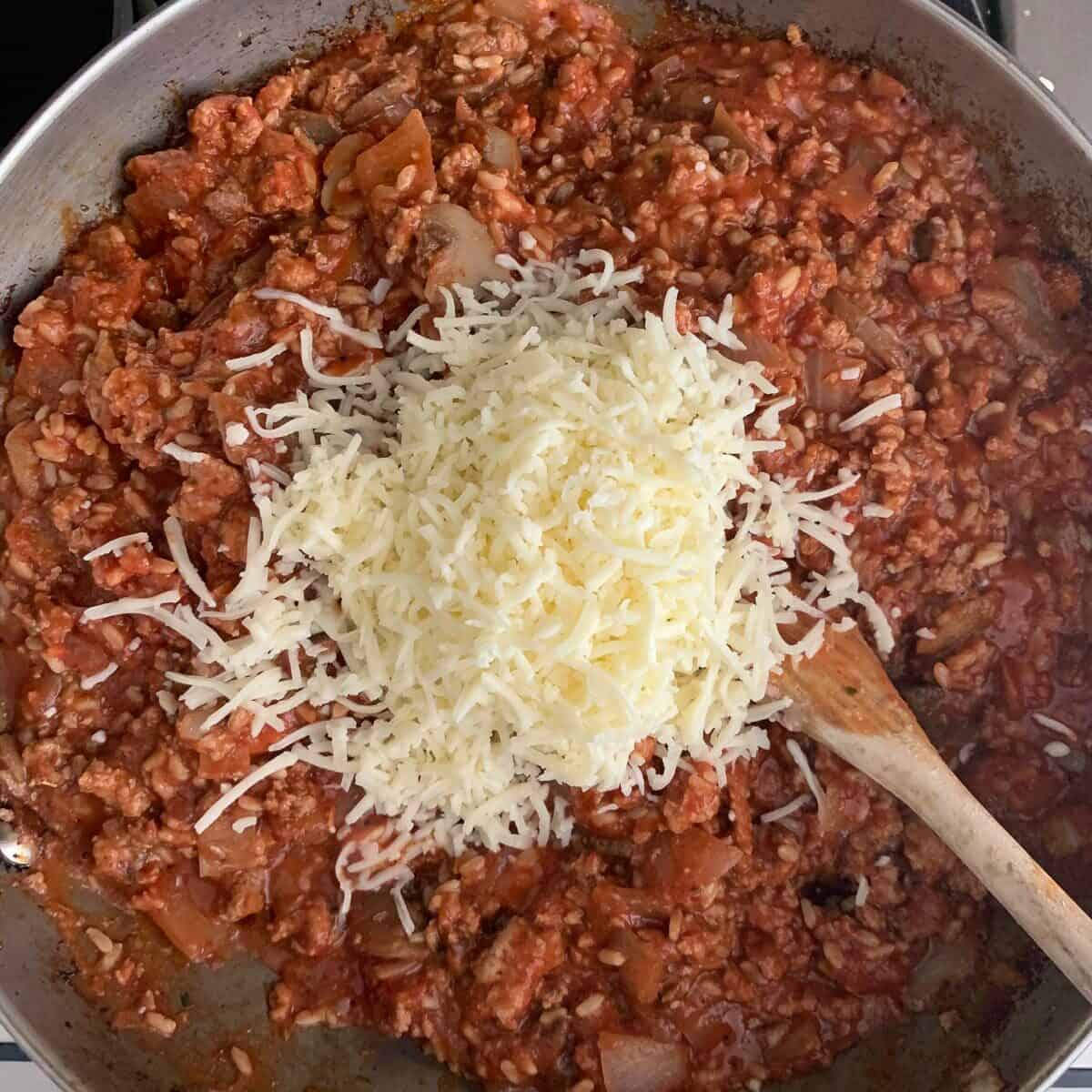 shredded mozzarella on top of ground turkey filling in pan on stove