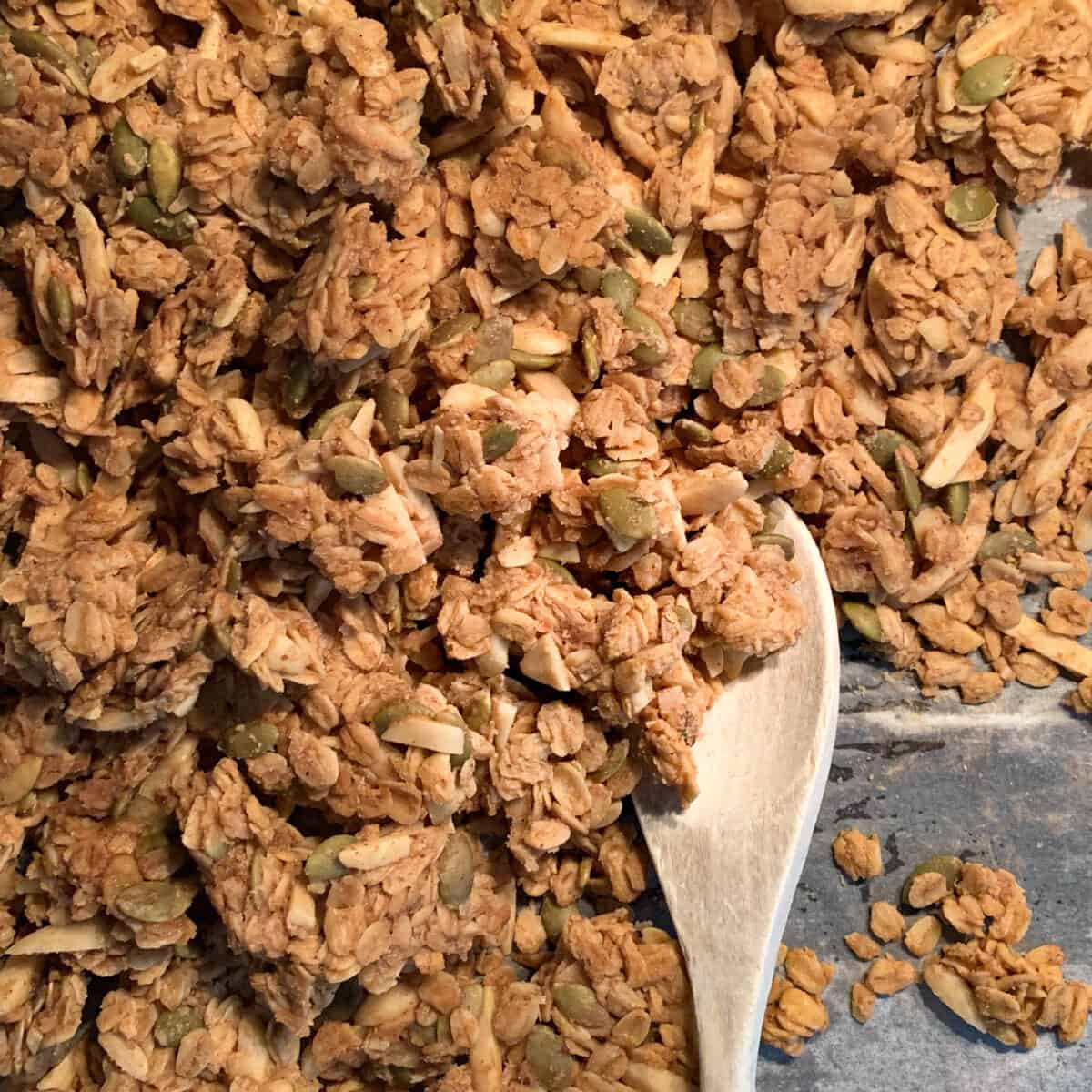 close up view of chunky homemade granola on parchment with wooden spoon