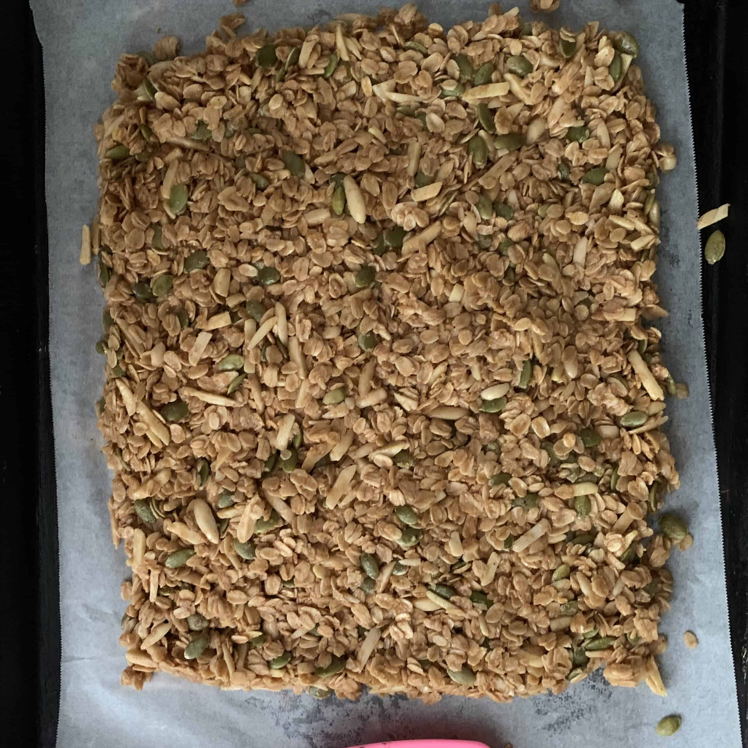 rectangle of raw granola patted down and ready to bake on parchment lined sheet