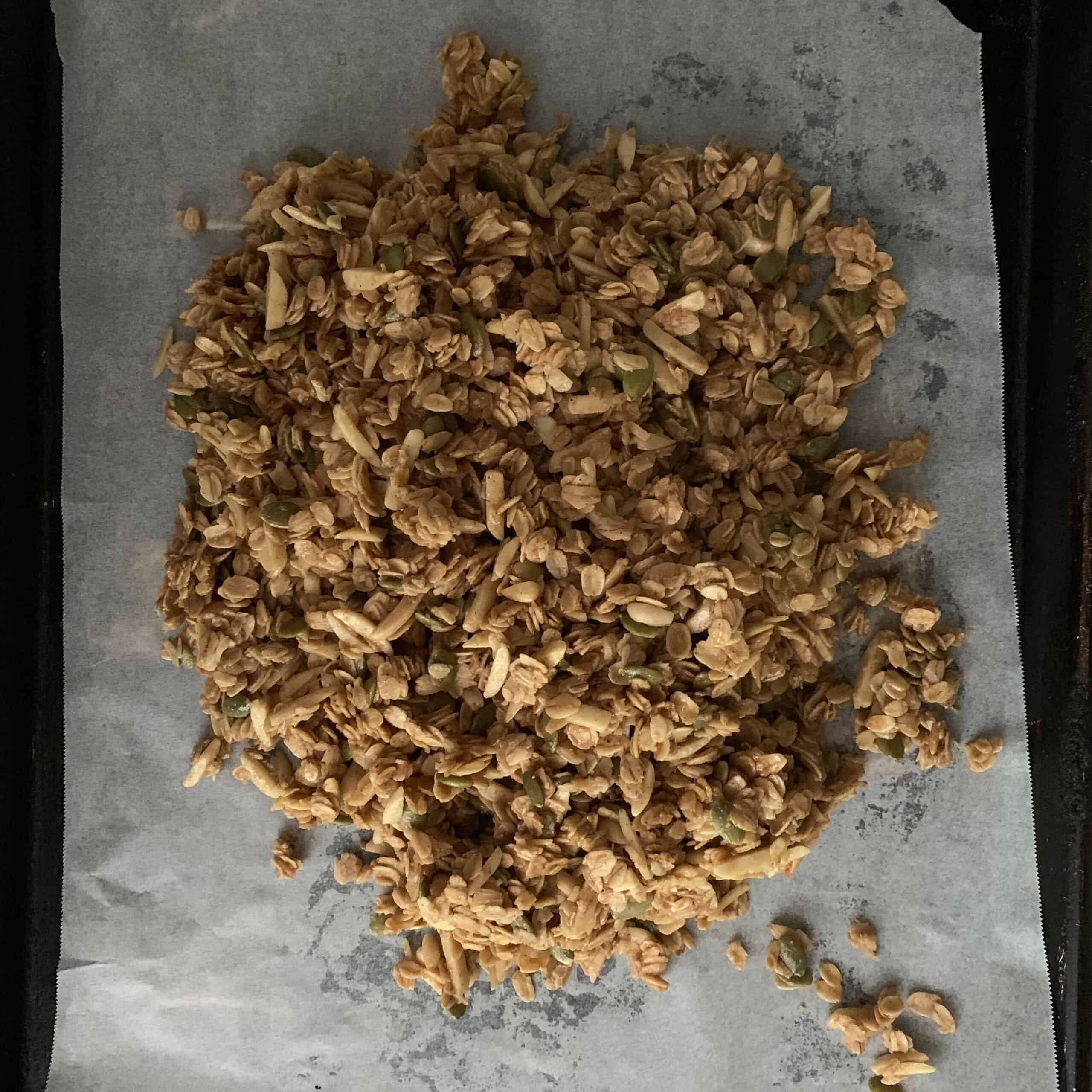 Raw granola poured onto parchment lined sheet ready to be flattened