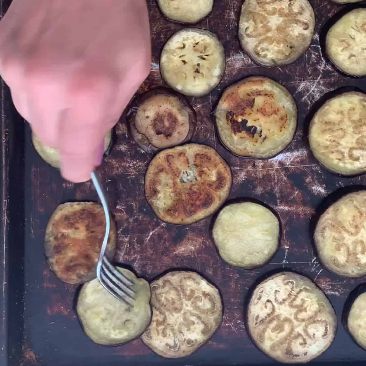 flipping eggplant slices to roast other side on black baking sheet