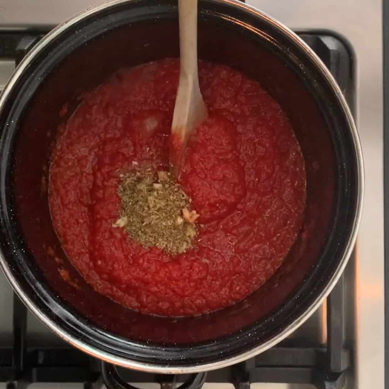 adding spices to marinara sauce on stovetop
