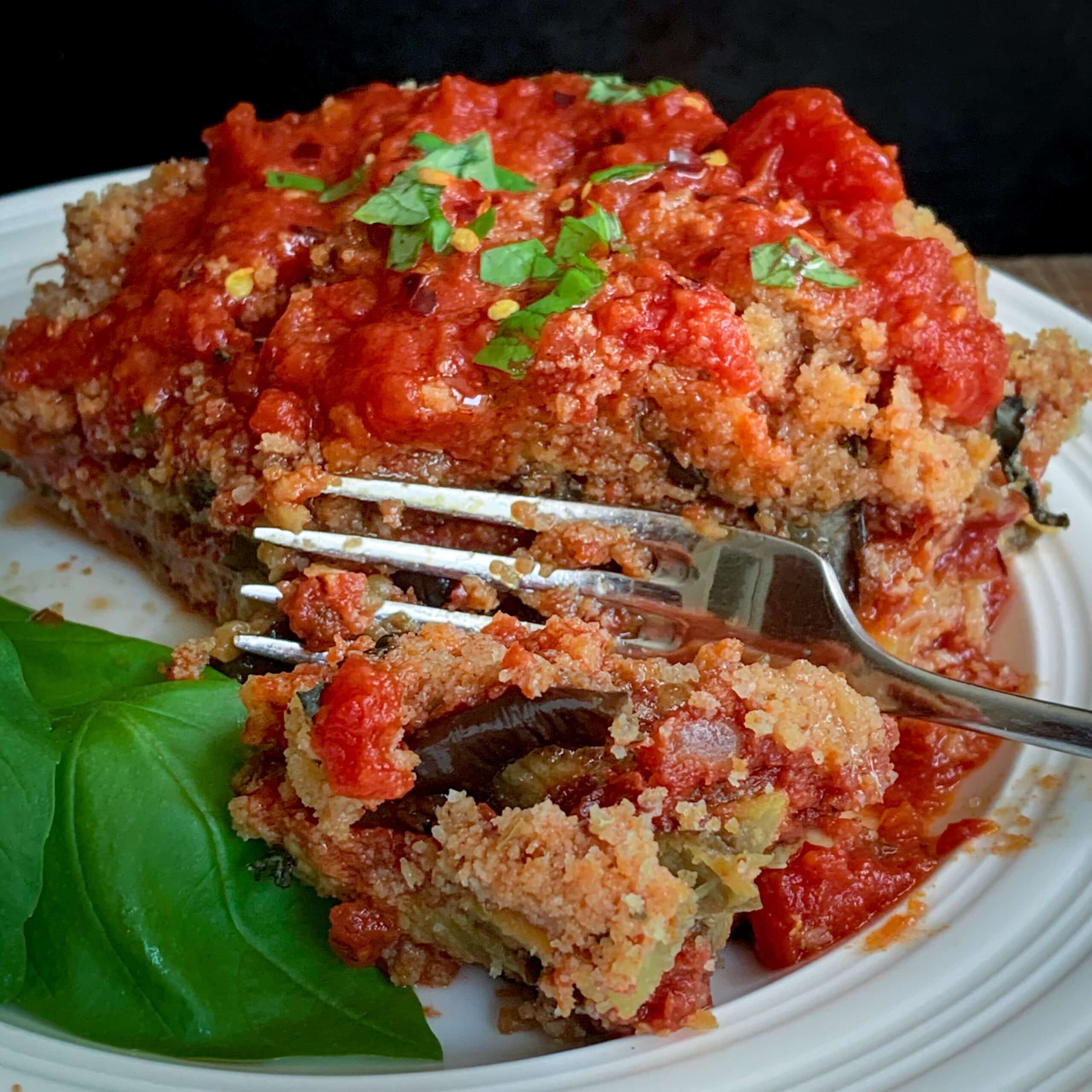 side view of baked eggplant parm with fork on white plate