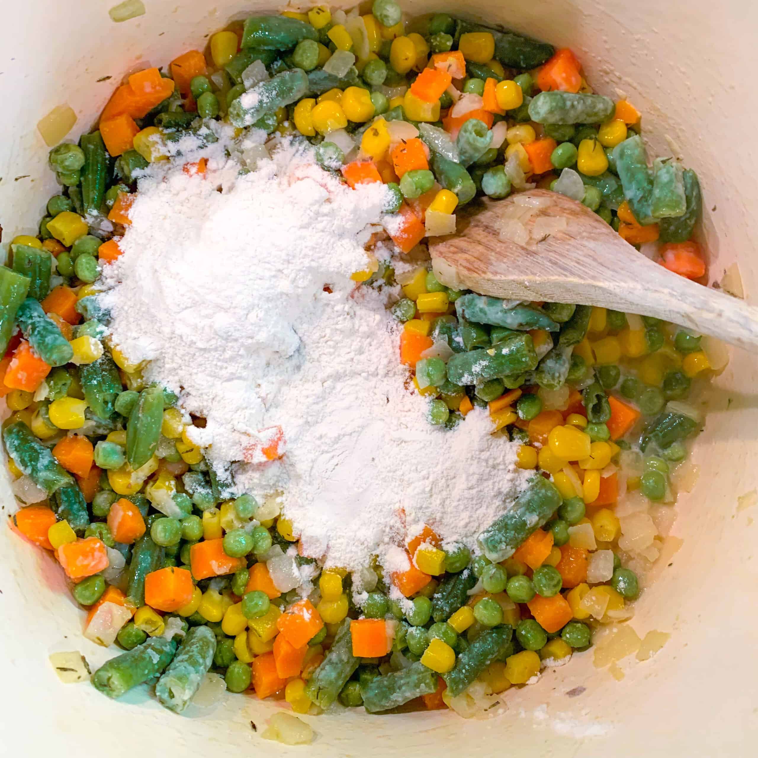 Flour with frozen veggies in pot with wooden spoon