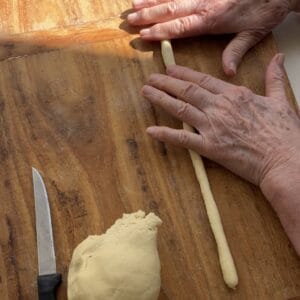 Rolling pasta dough into long rope on wooden board
